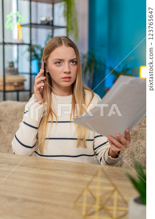 Caucasian woman solving problem on phone sitting at home, holding bills graphs, emotional worried Caucasian woman solving problem on phone sitting at home, holding bills graphs, emotional worried 123765647