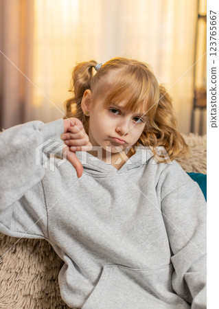 Young teenager girl showing thumbs down unhappy expression expressing disagreement indoors at home 123765667