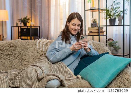 Smiling young woman in casual clothes text messaging on smartphone while lying on sofa at home Smiling young woman in casual clothes text messaging on smartphone while lying on sofa at home 123765669