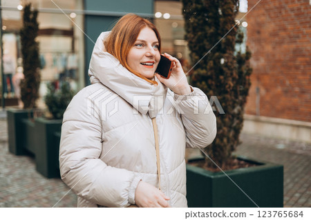 Happy 30s woman talking phone and look happy outdoors. Urban lifestyle concept. Winter time. Beautiful redhead woman walking on the city street. Happy 30s woman talking phone and look happy outdoors. Urban lifestyle concept. Winter time. Beautiful redhead woman walking on the city street. 123765684
