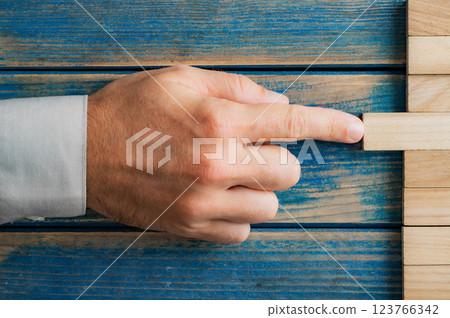Hand of caucasian businessman pushing a wooden peg into a stack of them Hand of caucasian businessman pushing a wooden peg into a stack of them 123766342