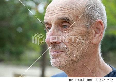 Bald Senior Man Smiles Slightly In The Nature Among The Trees Bald Senior Man Smiles Slightly In The Nature Among The Trees 123768627