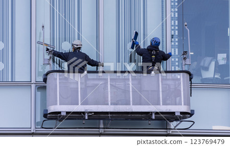 A worker cleaning windows in a gondola on a high-rise building A worker cleaning windows in a gondola on a high-rise building 123769479