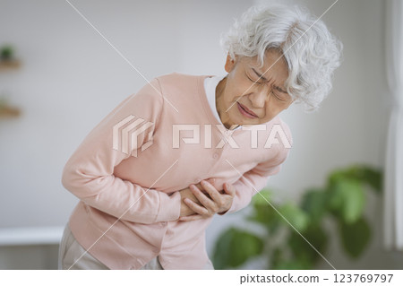 Senior woman suffering while holding her left chest Senior woman suffering while holding her left chest 123769797