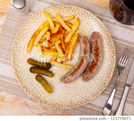 Fried sausages with served with french fries potatoes and marinated cucumbers closeup Fried sausages with served with french fries potatoes and marinated cucumbers closeup 123770071