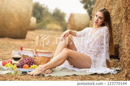 Woman in transparent dress and white lingerie posing at picnic near bale of hay 123770144