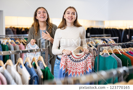 Positive young women friends choosing winter sweater in fashion store Positive young women friends choosing winter sweater in fashion store 123770165