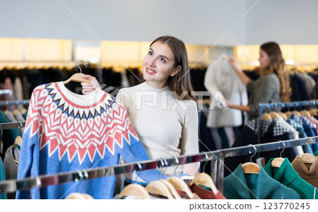Smiling female in casual outfit admiring pullover with a pattern in a showroom 123770245