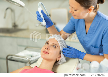 Adult woman cosmetologist doing moisturizing procedure to young woman 123770282