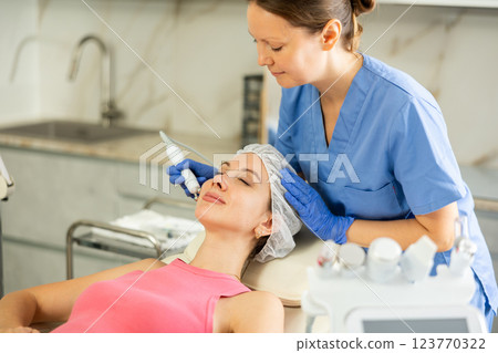 Adult woman cosmetologist doing microcurrent procedure to young woman Adult woman cosmetologist doing microcurrent procedure to young woman 123770322
