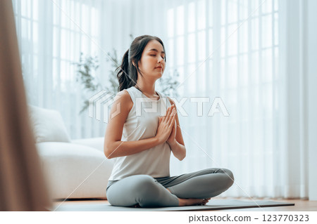 Young Asian woman meditating in lotus position at home Young Asian woman meditating in lotus position at home 123770323