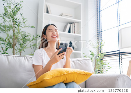 Happy young asian woman relax on comfortable couch at home texting messaging on smartphone 123770328