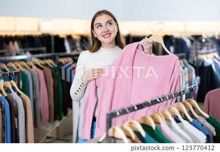 Dreamy female in casual outfit holding a pink buttonless jacket while shopping in a mall Dreamy female in casual outfit holding a pink buttonless jacket while shopping in a mall 123770412