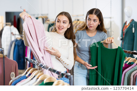 Two young women comparing green and pink cardigans while spending time together in a shopping mall Two young women comparing green and pink cardigans while spending time together in a shopping mall 123770414