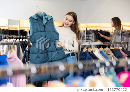 Young woman choosing insulated vest in store Young woman choosing insulated vest in store 123770422