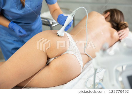 Young woman getting ultrasound cavitation body contouring treatment, anti-cellulite therapy, massage and and moisturizing bottom layer of skin from female cosmetologist. Hardware cosmetology for body Young woman getting ultrasound cavitation body contouring treatment, anti-cellulite therapy, massage and and moisturizing bottom layer of skin from female cosmetologist. Hardware cosmetology for body 123770492