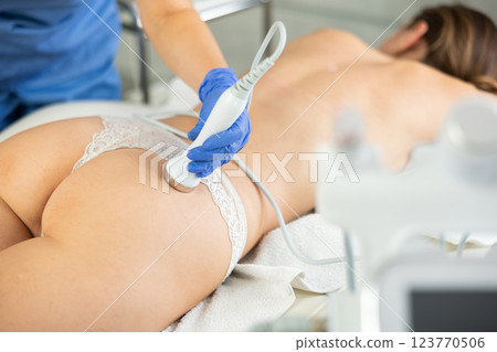 Adult woman cosmetologist gives ultrasonic massage of butt to young woman 123770506