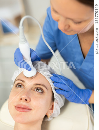 Adult woman cosmetologist doing ultrasound procedure to young woman 123770549