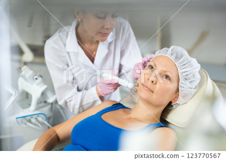 Young doctor doing RF lifting procedure for face lifting of adult woman laying in spa center. Smoothes wrinkles and tightens skin machine Young doctor doing RF lifting procedure for face lifting of adult woman laying in spa center. Smoothes wrinkles and tightens skin machine 123770567