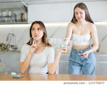 Thoughtful mother sitting at the kitchen table giving money to daughter 123770657