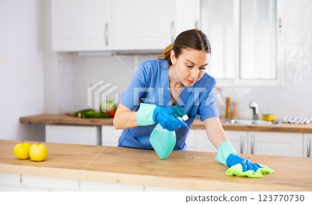 Young woman professional cleaner cleaning desk with detergents in kitchen Young woman professional cleaner cleaning desk with detergents in kitchen 123770730