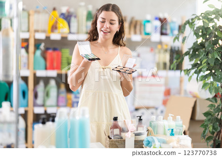 Smiling young woman examining makeup palettes in store 123770738