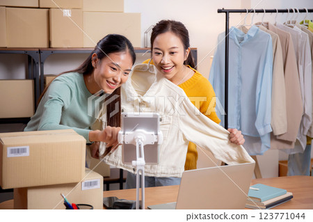 Two young asian woman live online clothing store while showing clothing with tablet on social. Two young asian woman live online clothing store while showing clothing with tablet on social. 123771044