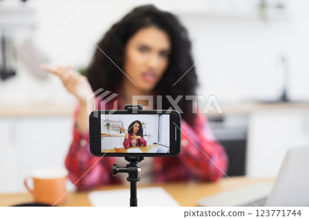 African woman in casual outfit recording video for social media in kitchen, smartphone on tripod, relaxed atmosphere. African woman in casual outfit recording video for social media in kitchen, smartphone on tripod, relaxed atmosphere. 123771744