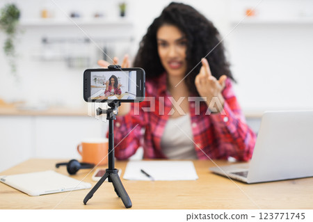 African woman in casual outfit recording video for social media in kitchen, smartphone on tripod, relaxed atmosphere. African woman in casual outfit recording video for social media in kitchen, smartphone on tripod, relaxed atmosphere. 123771745