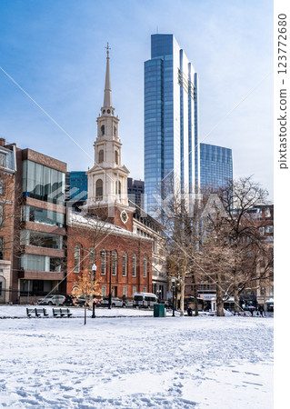 View of Park Street Church and surrounded buildings in Boston during winter with snow on the Boston Common ground and flock of birds flying against clear blue sky 123772680