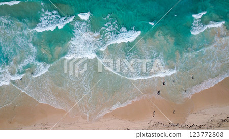 Aerial view of a sandy beach with turquoise waves crashing onto the shore scattered people are seen walking along the coastline 123772808