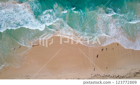 Aerial view of turquoise waves gently crashing onto a sandy beach. The oceans clear water, mixed with white foam, creates a tranquil Aerial view of turquoise waves gently crashing onto a sandy beach. The oceans clear water, mixed with white foam, creates a tranquil 123772809