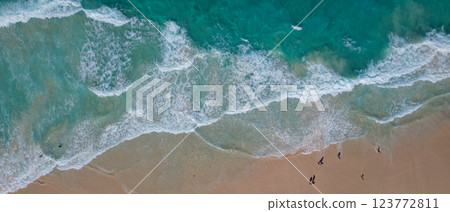 Aerial view of turquoise waves gently crashing onto a sandy beach. The oceans clear water, mixed with white foam, creates a tranquil Aerial view of turquoise waves gently crashing onto a sandy beach. The oceans clear water, mixed with white foam, creates a tranquil 123772811