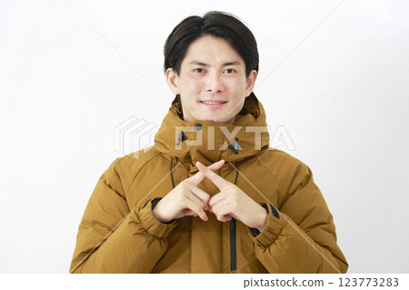 一名身穿羽絨外套的男子在白色背景上做出十字架的手勢 123773283