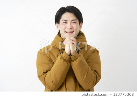 A man wearing a down jacket prays on a white background, looking at the camera 123773308