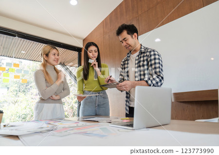 Diverse design team discussing project ideas using digital tablet in modern office. 123773990