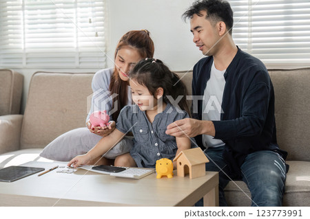Parents teaching their daughter about saving money with piggy banks 123773991