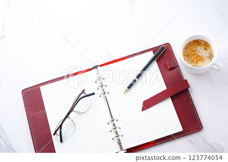 An image of a man sipping a cafe latte while working at his desk with a wine-red leather organizer 123774054