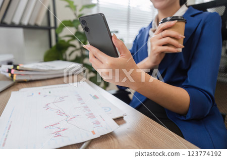Businesswoman reviewing financial reports on smartphone while holding coffee 123774192