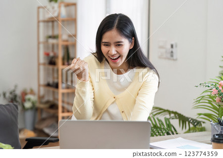 Excited businesswoman celebrating success in home office while working on laptop. 123774359