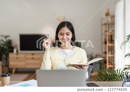 Inspiring woman holding a light bulb and book, celebrating a new idea at home office Inspiring woman holding a light bulb and book, celebrating a new idea at home office 123774830