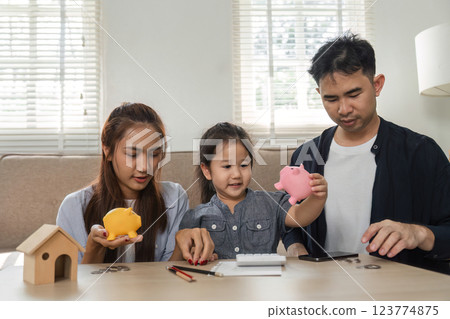 Family engaging in saving activities with piggy banks and a calculator at home 123774875
