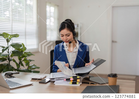 Detail-oriented accountant organizing tax paperwork while consulting clients in a modern office. 123774881