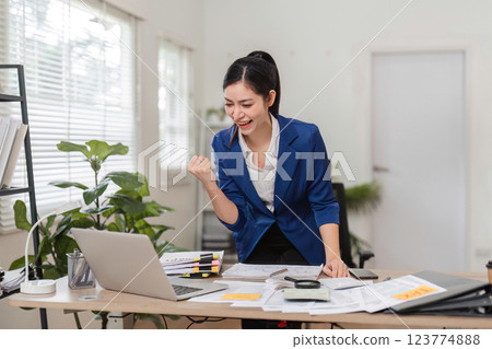 Excited businesswoman celebrating success while managing finances at her desk. Excited businesswoman celebrating success while managing finances at her desk. 123774888