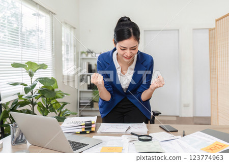 Businesswoman triumphantly celebrating her financial success and celebrating financial achievements at her desk 123774963