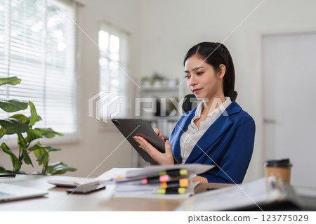 Accountant engaged with financial documents and tablet in a well-lit office. 123775029
