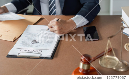 Lawyer signing contract document at desk, preparing legal agreement with gavel and scales of justice nearby. 123775067