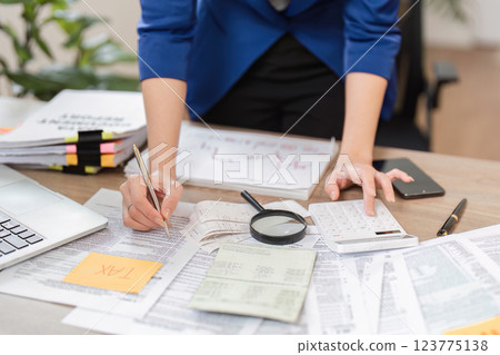 Businesswoman calculating taxes and managing finances at her desk with paperwork and calculator. 123775138