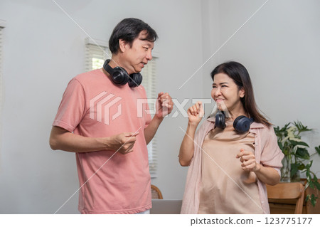 Playful middle-aged couple enjoying music and dancing indoors with headphones. Playful middle-aged couple enjoying music and dancing indoors with headphones. 123775177