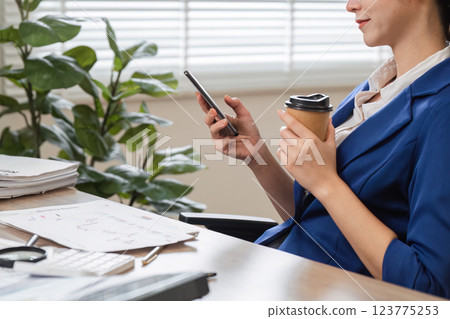 Accountant checking phone while enjoying coffee in a modern office. 123775253